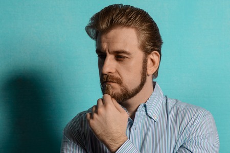 Portrait of an attractive bearded man with hair in the style of rockabilly in a striped shirt. As for the arm beard blue wallの写真素材