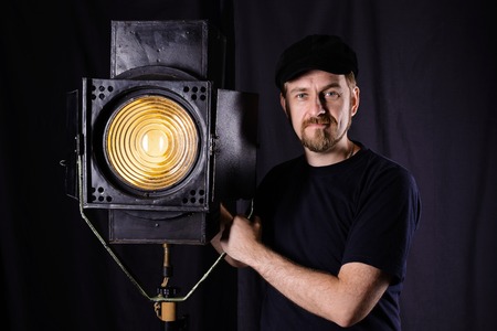 Man wearing a cap stands near a stage spotlight on black backgroundの写真素材