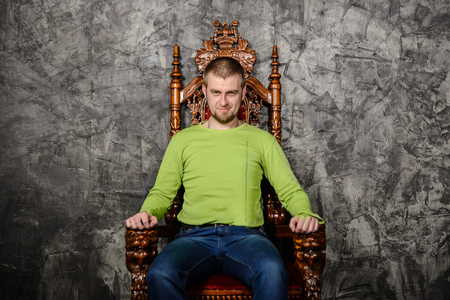 Attractive young man in a light green t-shirt sitting on the throne and smiling looking at the cameraの写真素材