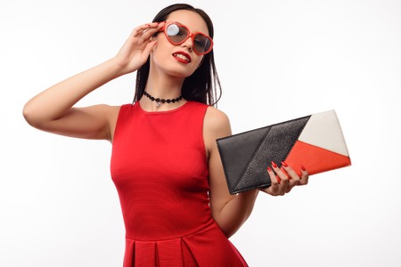 Stylish girl in red dress and clutch holds on to sunglasses in the shape of heart.の写真素材