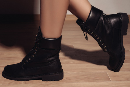 autumn black women's boots dressed the girl standing on the wooden floor near the wallの写真素材
