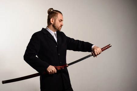 Male businessman wearing a suit pulls out a sword of Japanese samuraiの写真素材