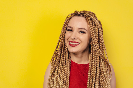 Beautiful hipster smile girl with pigtails wearingred dress posing on yellow background.の写真素材