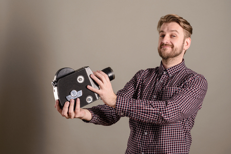 Young attractive cameraman in a plaid shirt takes himself off to an old movie camera.の写真素材