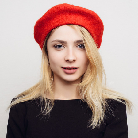 Portrait of a young blond woman in a red beret on a white background.の写真素材