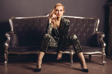 Beautiful young woman in a velor suit sits on a gray vintage couch.の写真素材