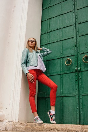 Fashionable young model girl in vintage fashion jacket with jeans and Glasses posing near green old...