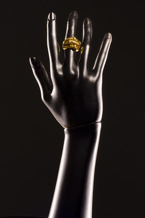 Black plastic hand of a mannequin on a black background with a gold ring on her finger isolated dark background at the studio.の写真素材