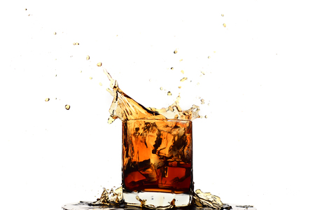 Ice cube falling into whiskey in glass isolated on whiteの写真素材