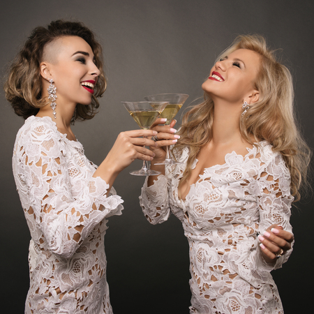 two beautiful young women girlfriends in white short dress celebrate the holiday with martini glasses isolatedの写真素材
