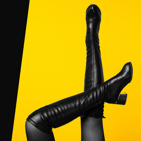 Sexy legs wearing black leather boots on yellow background - Imageの写真素材