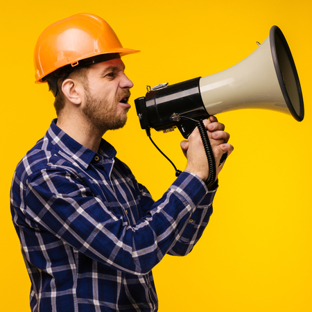 Angry worker man in orange helmet with a megaphone on yellow background - Imageの写真素材
