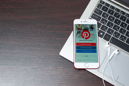 Tula, Russia, March 12, 2019: the button to log in Pinterest on the iphone screen is placed on the laptop keyboard next to EarPods. Pinterest is an online pinboard that allows people to pin their interesting things. - Imageのeditorial素材