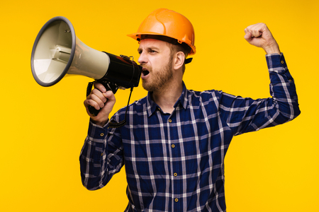 Angry worker man in orange helmet with a megaphone on yellow background - Imageの写真素材
