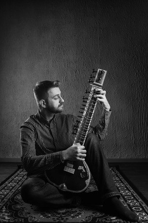 Portrait of a European man playing the sitar sitting on the carpet- Imageの写真素材