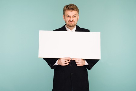 Angry beard young business man showing blank signboard, on blue backgroundの写真素材