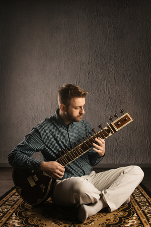 Portrait of a European man playing the sitar sitting on the carpet- Imageの写真素材