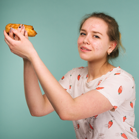 Portrait of pimply teen girl wants to eat eclair cake on blue backgroundの写真素材