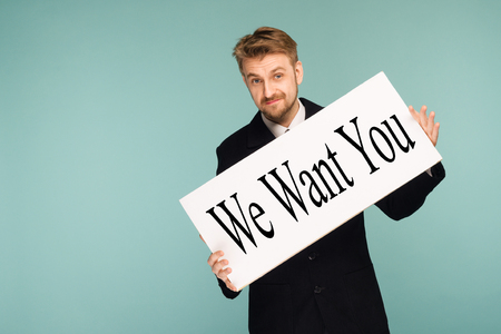 Happy smiling young business man showing signboard with sign We Want You, on blue backgroundの写真素材