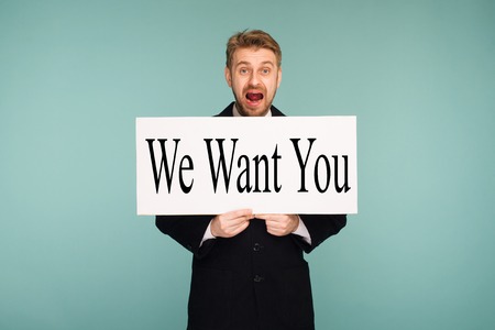 Spacey mature business man showing signboard with sign We Want You, on blue backgroundの写真素材
