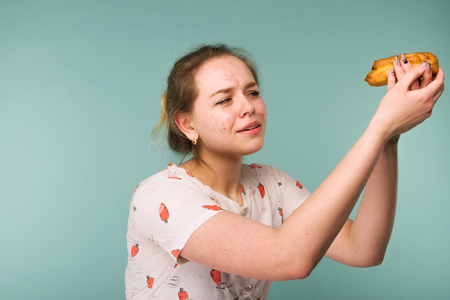 Portrait of pimply teen girl wants to eat eclair cake on blue backgroundの写真素材