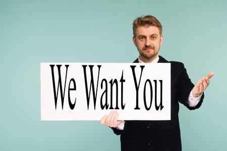 Happy smiling young business man showing signboard with sign We Want You, on blue backgroundの写真素材