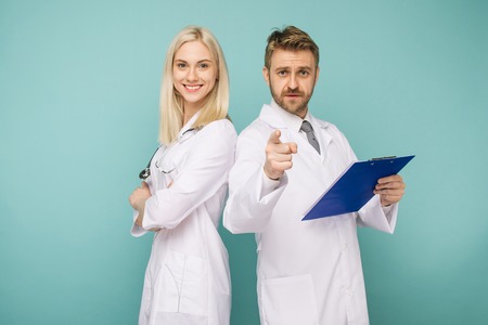 Happy medical team of doctors, man pointing to camera and smiling woman, isolated over blue backgroundの写真素材
