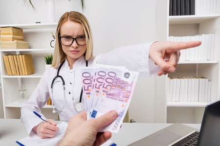 Woman doctor with stethoscope refusing bribes or kickbacks, currencies euro, patient giving money for medical services, concept of corruption - Imageの写真素材