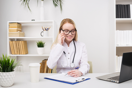 Portrait of a beautiful smiling woman doctor while talking on the smartphone and complete a medical information - Imageの写真素材