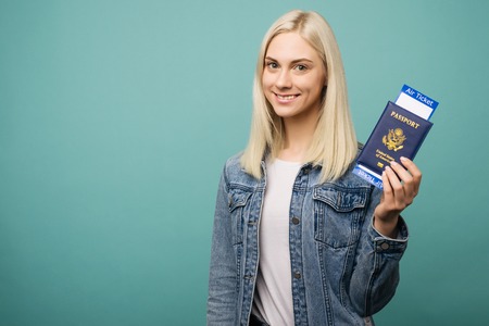 Portrait of a cheerful cute american girl traveller showing passport with tickets isolated over blue backgroundの写真素材