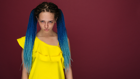 Portrait of a unhappy girl with freckles and blue braided hair against a ruby backgroundの写真素材