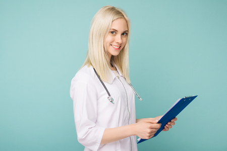 Portrait of an attractive young female doctor in white coat on blue backgroundの写真素材