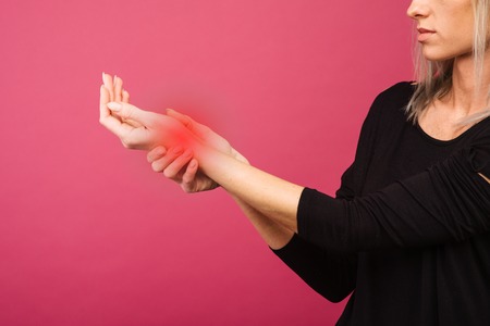 Female holding hand to spot of wrist pain. Concept photo with Color Enhanced skin with read spot indicating location of the pain.の写真素材