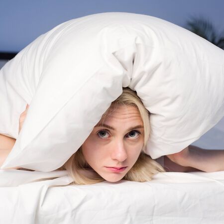 Female lying on bed and closing her ears with pillow - imageの写真素材