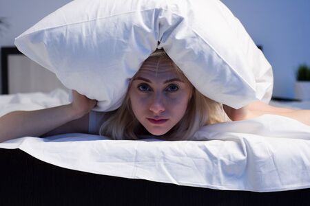 Female lying on bed and closing her ears with pillow - imageの写真素材