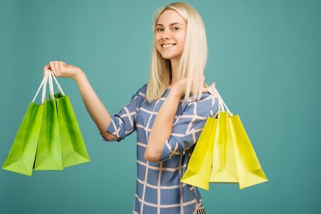 Happy girl in a checkered blouse holds shopping bags on blue backgroundの写真素材