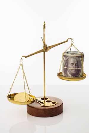 Bitcoin value increase trend. The coin outweighs the balance. On another bowl a stack of hundred dollar bills. White background - imageの写真素材