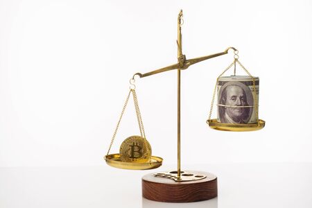 Bitcoin value increase trend. The coin outweighs the balance. On another bowl a stack of hundred dollar bills. White background - imageの写真素材