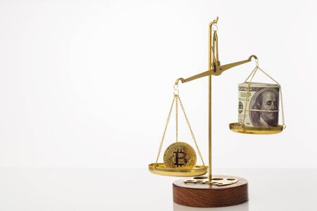 Bitcoin value increase trend. The coin outweighs the balance. On another bowl a stack of hundred dollar bills. White background - imageの写真素材