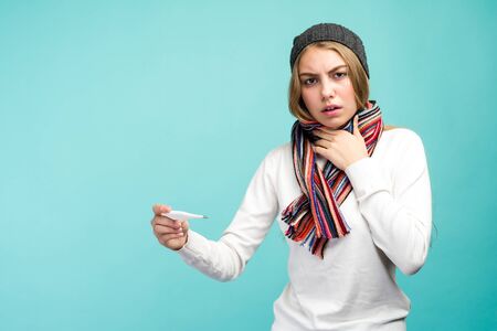Sad teen girl having flue taking thermometer against blue background. Beautiful lady is sick with a high temperature, isolated close-up. - imageの写真素材
