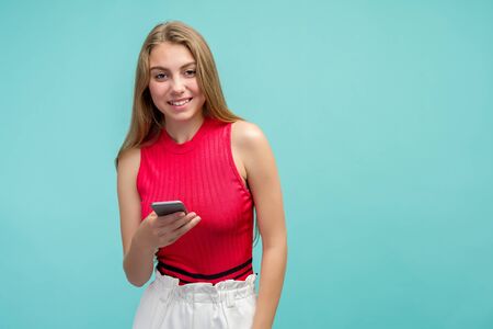 Overjoyed happy excited female glad to recieve text message informing about salary, rejoices good news, stares at mobile phone, gestures actively from happiness, stands indoor alone. Reaction conceptの写真素材