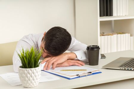 Tired asian businessman sleeping in office. Middle eastern business man worked late and fell asleep on the table. Creative casual gay sleeping at his working place, woke up.の写真素材