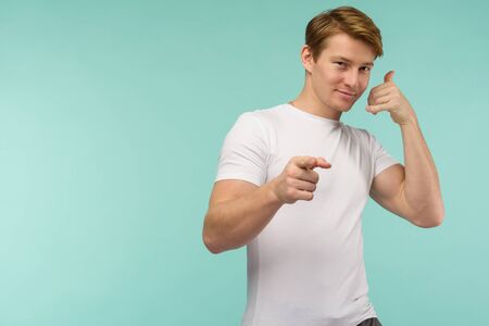 Call me. Handsome young smiling man looking at camera and gesturing mobile phone near face while...