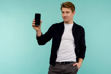 Cheerful sporty red-haired guy shows the smartphone screen on a blue background. - imageの写真素材