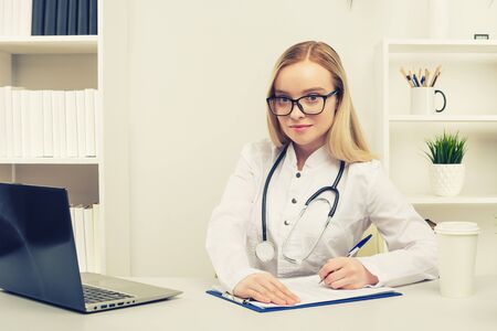 Young beautiful doctor woman working happy and smile in hospital, sitting on table, medical concept, tonedの写真素材
