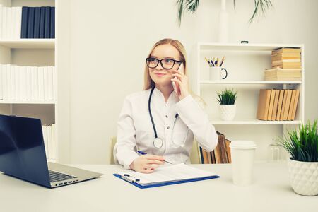Portrait of a beautiful smiling woman doctor while talking on the smartphone and complete a medical information - Image tonedの写真素材
