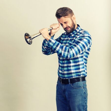 Bearded man in a plaid shirt looks at the horn isolated on grey background