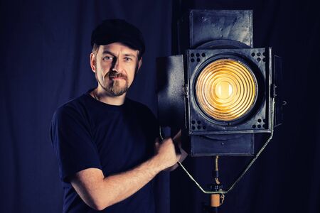 Man wearing a cap stands near a stage spotlight on black background