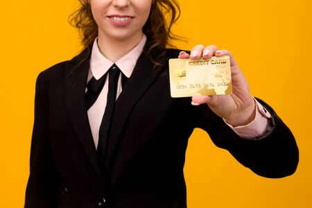 Portrait of a beautiful young business woman standing isolated over yellow background, holding credit card - imageの写真素材
