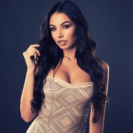 portrait of beautiful young woman with long hair in a tight shiny dress on dark backgroundの写真素材